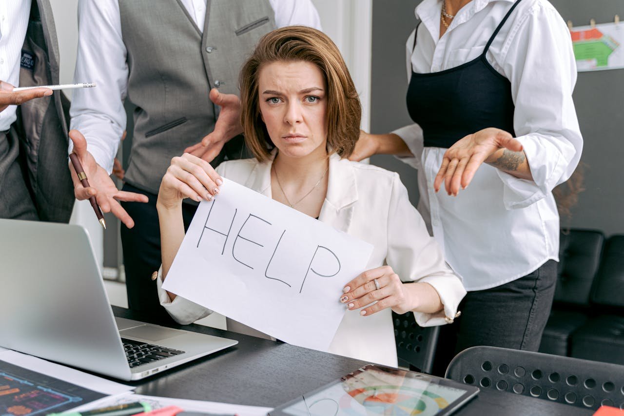 Stressed office worker holding a help sign surrounded by colleagues' demands.